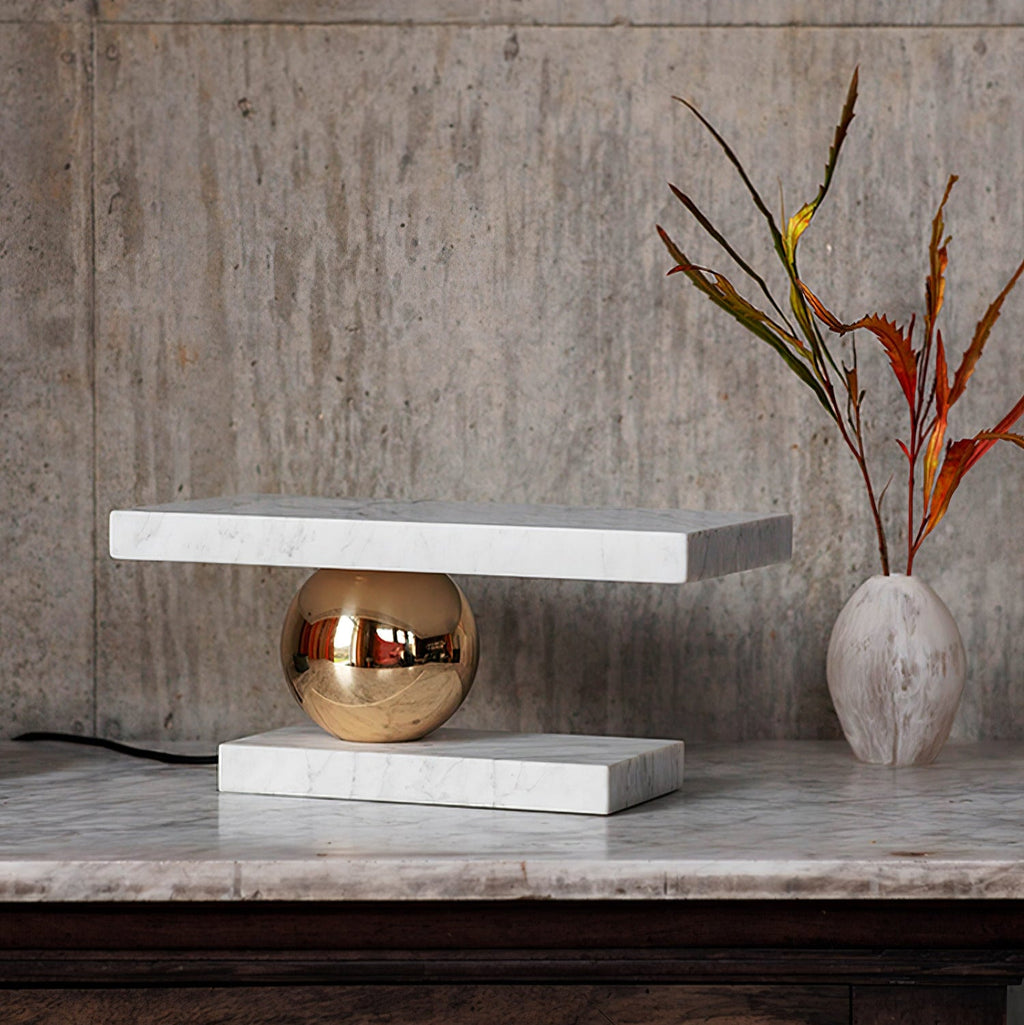 Clérachic white marble table lamp glowing on a marble ledge beside a ceramic vase with dried branches.
