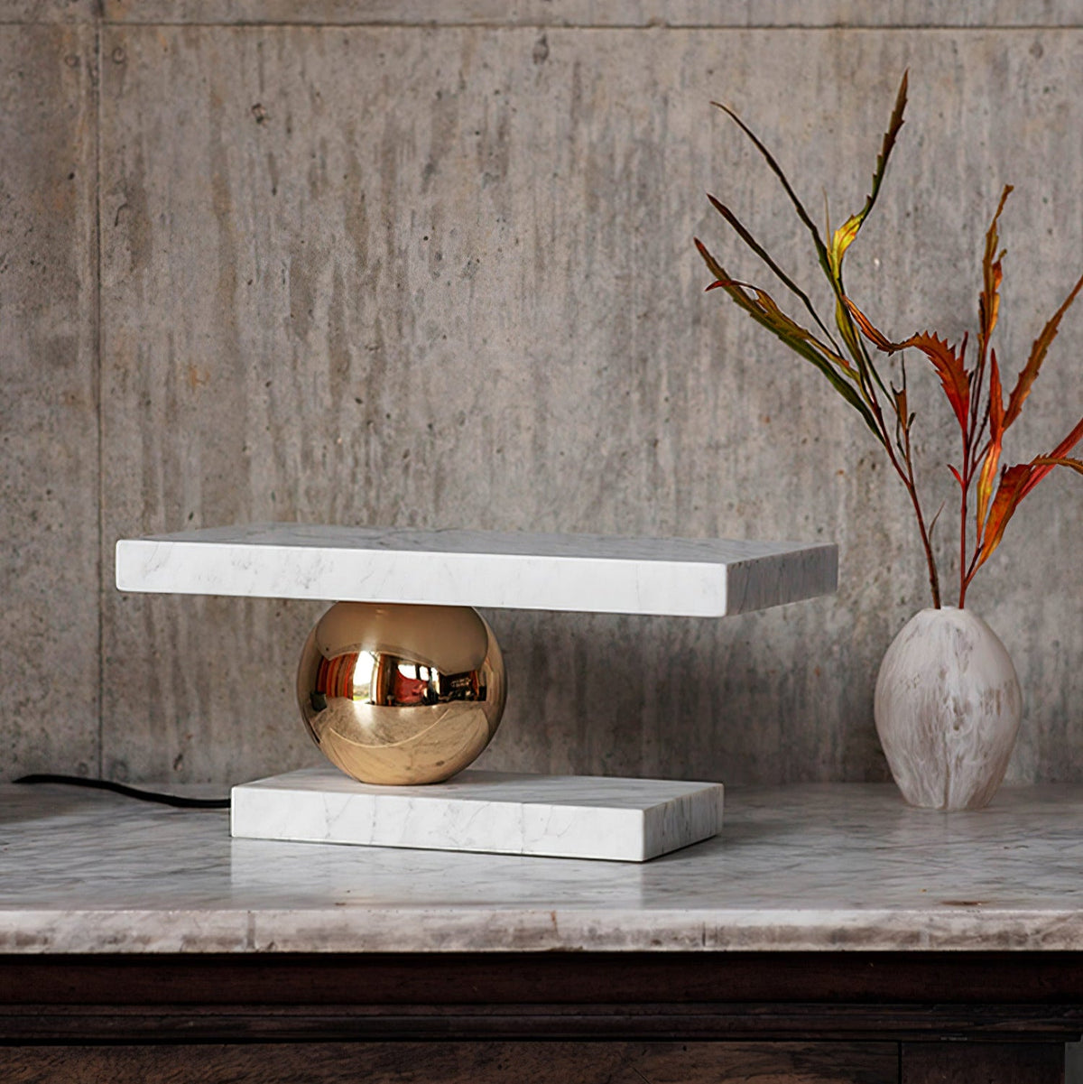 Clérachic white marble table lamp glowing on a marble ledge beside a ceramic vase with dried branches.