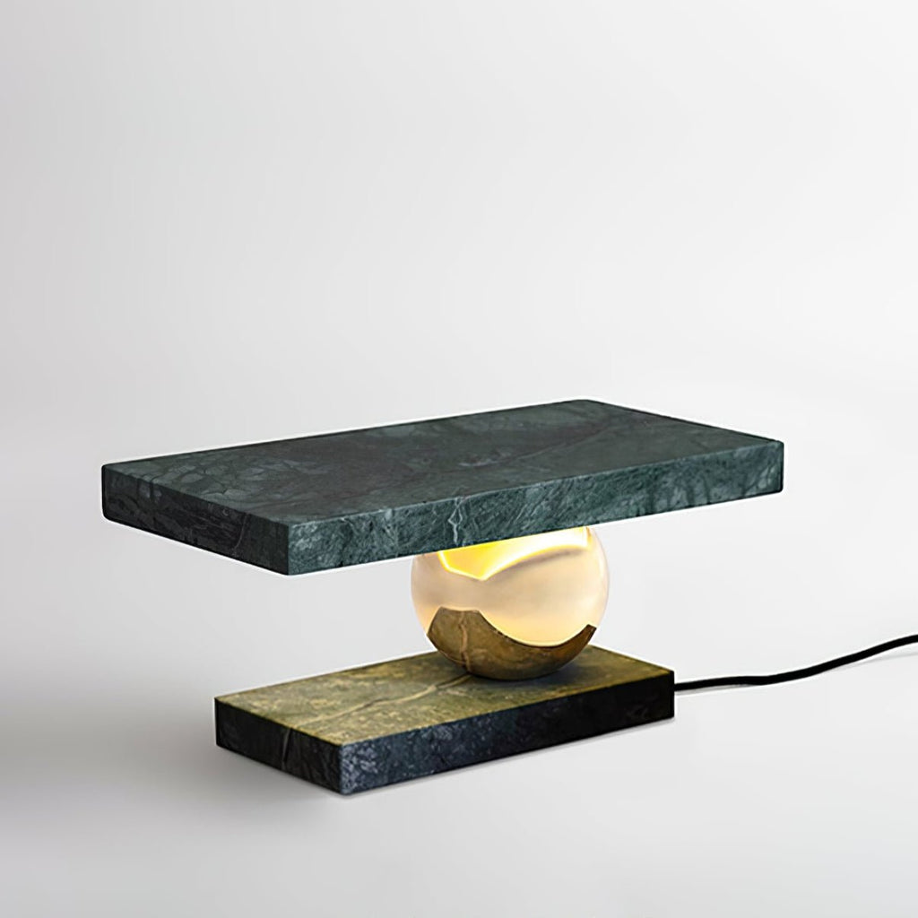 Clérachic green marble table lamp glowing in close-up against a white studio backdrop, the brass sphere catching the light.