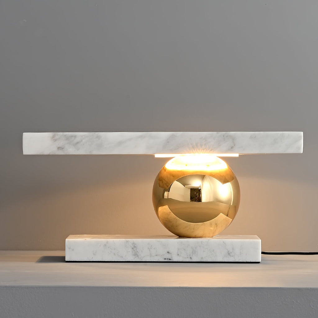 Clérachic white marble table lamp glowing on a grey tabletop, shot close to show the brass sphere and cord.