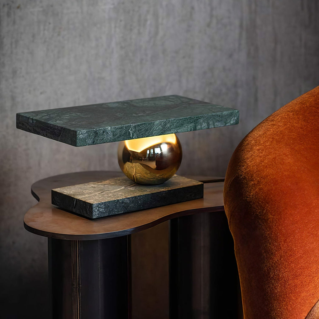 Clérachic green marble table lamp glowing on a wooden side table beside a burnt-orange velvet armchair, seen from a lower angle.