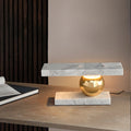 A notebook sits on the wooden desk beside the Clérachic white marble lamp, a wood-slat wall behind it.