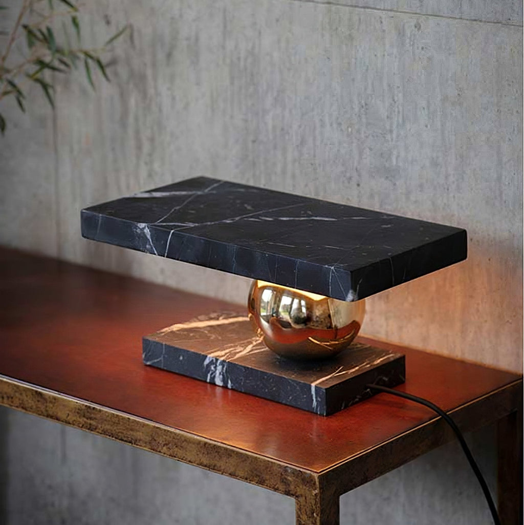 Against a concrete wall, the Clérachic black marble lamp glows on its reddish leather-topped console table.