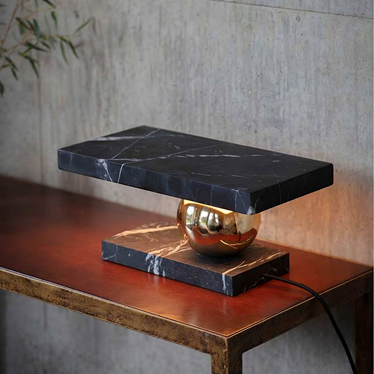 Against a concrete wall, the Clérachic black marble lamp glows on its reddish leather-topped console table.