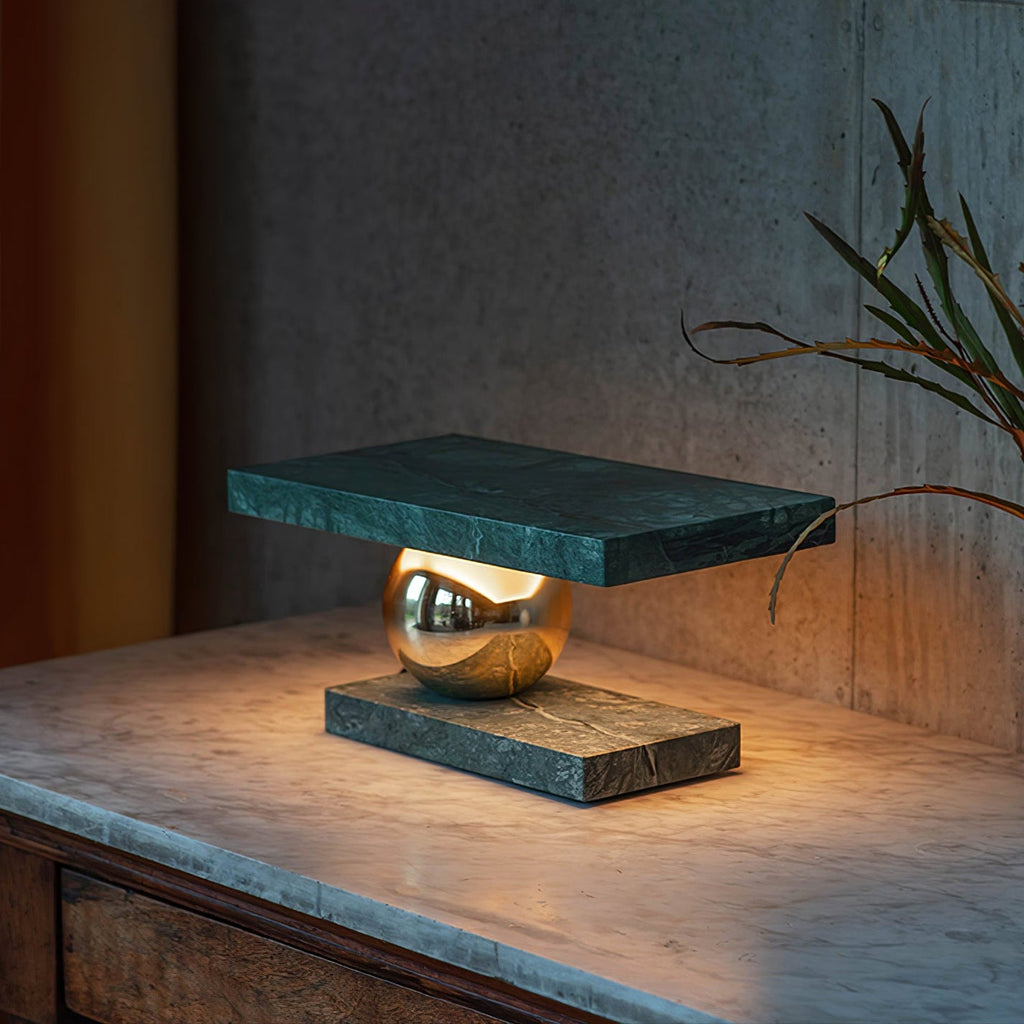 A bare branch in a vase sits beside the Clérachic green marble lamp on its blue-grey marble surface.