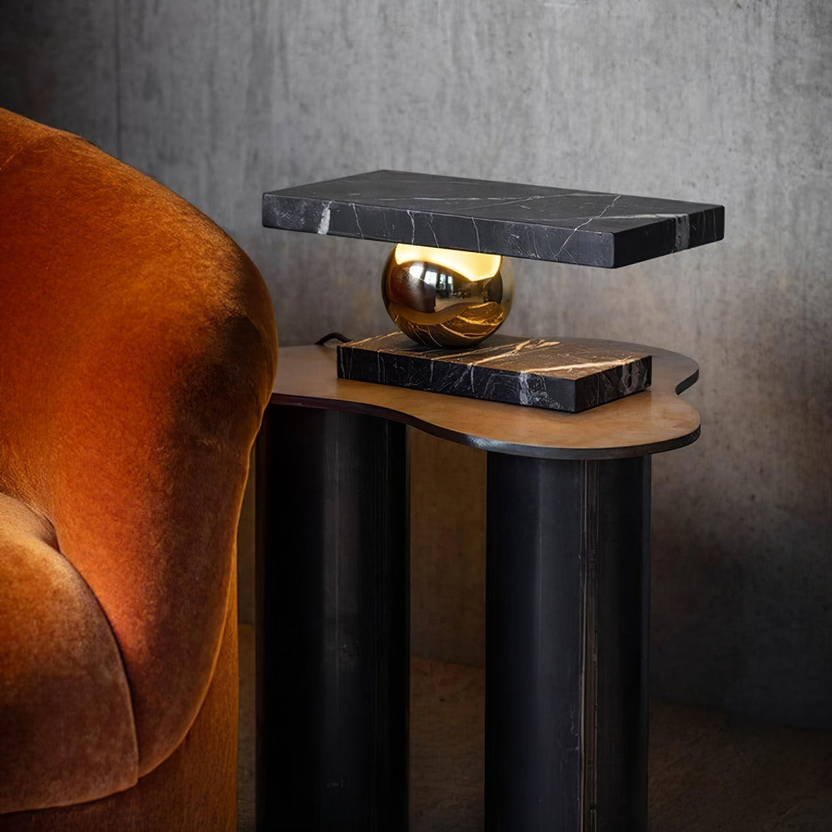 Clérachic black marble table lamp glowing on a wooden side table next to a burnt-orange velvet armchair.