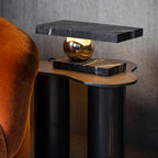 Clérachic black marble table lamp glowing beside the same armchair, framed in a wider view of the room.