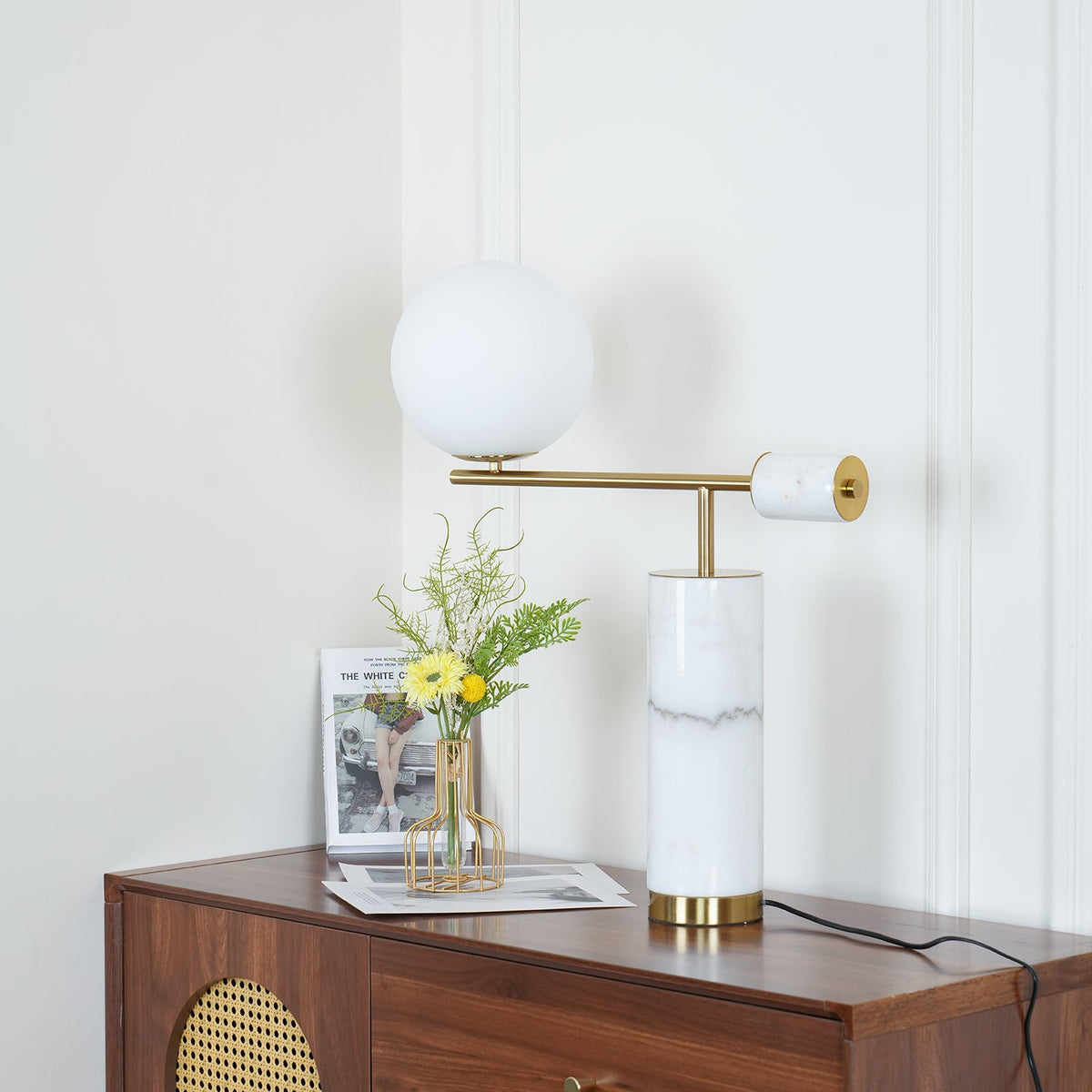 Cropped close on the dresser, the Clérachic lamp's marble finial and brass disc are sharp while the magazine blurs softly.