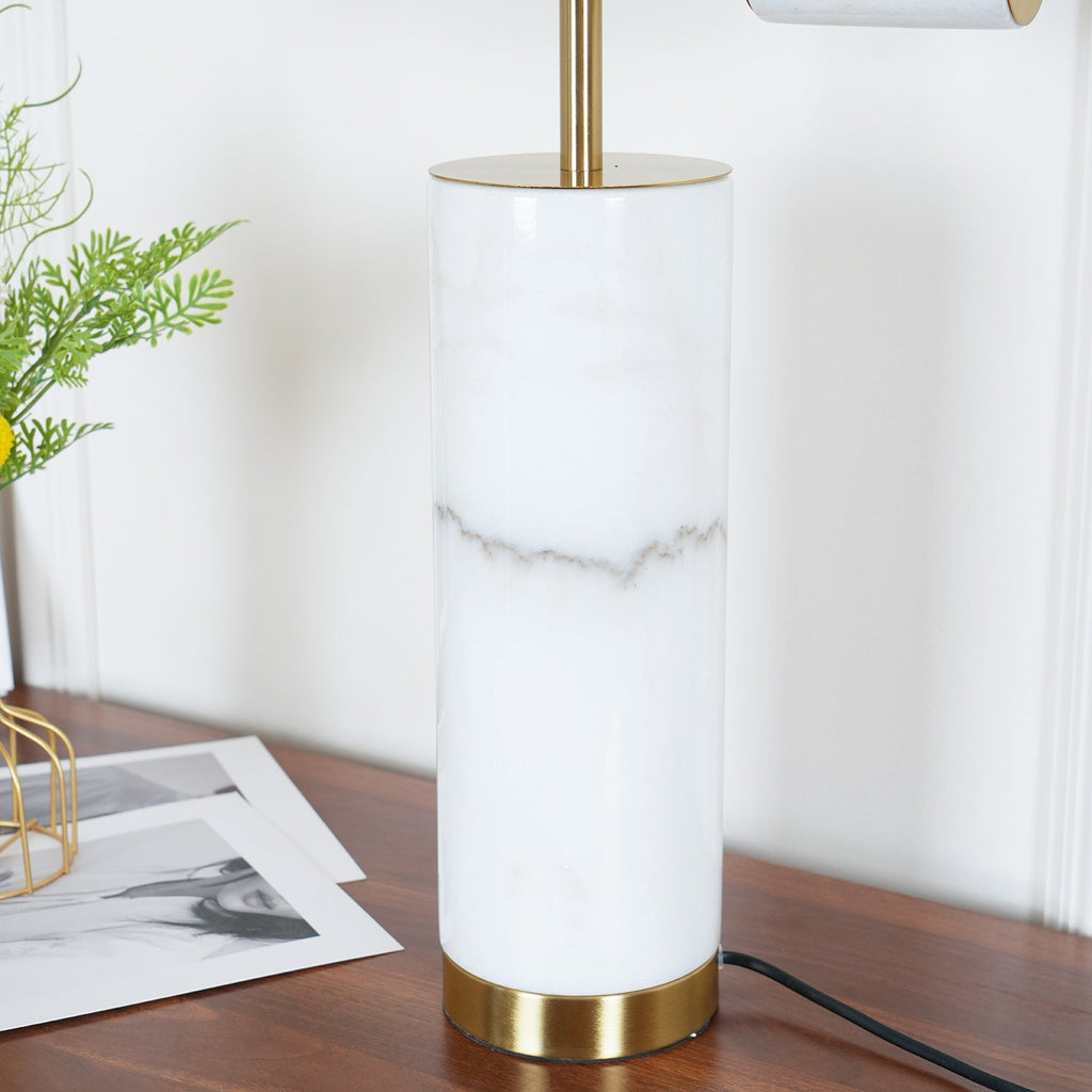 A close-up of the Clérachic lamp's white marble column and brass base ring, a sprig of greenery blurred in the corner.