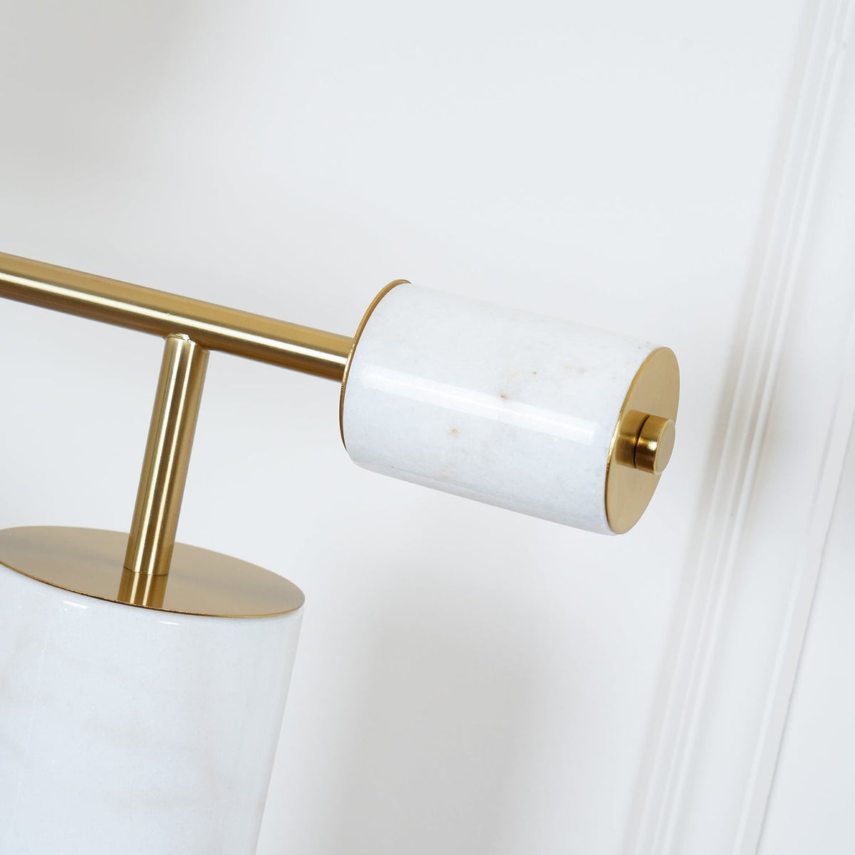 An extreme close-up of the Clérachic lamp's brass stem meeting its white marble disc cap, a second column blurred behind.