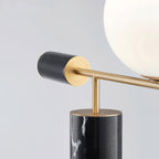 A detail shot of the Clérachic lamp's brass stem meeting its round base plate, the glass globe softly blurred above.