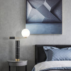 The lit Clérachic lamp glows beside a grey upholstered bed, an abstract framed print hanging on the wall above it.