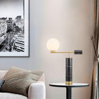 A Clérachic table lamp rests unlit on a round side table beside a beige sofa, a black-and-white cityscape print behind it.