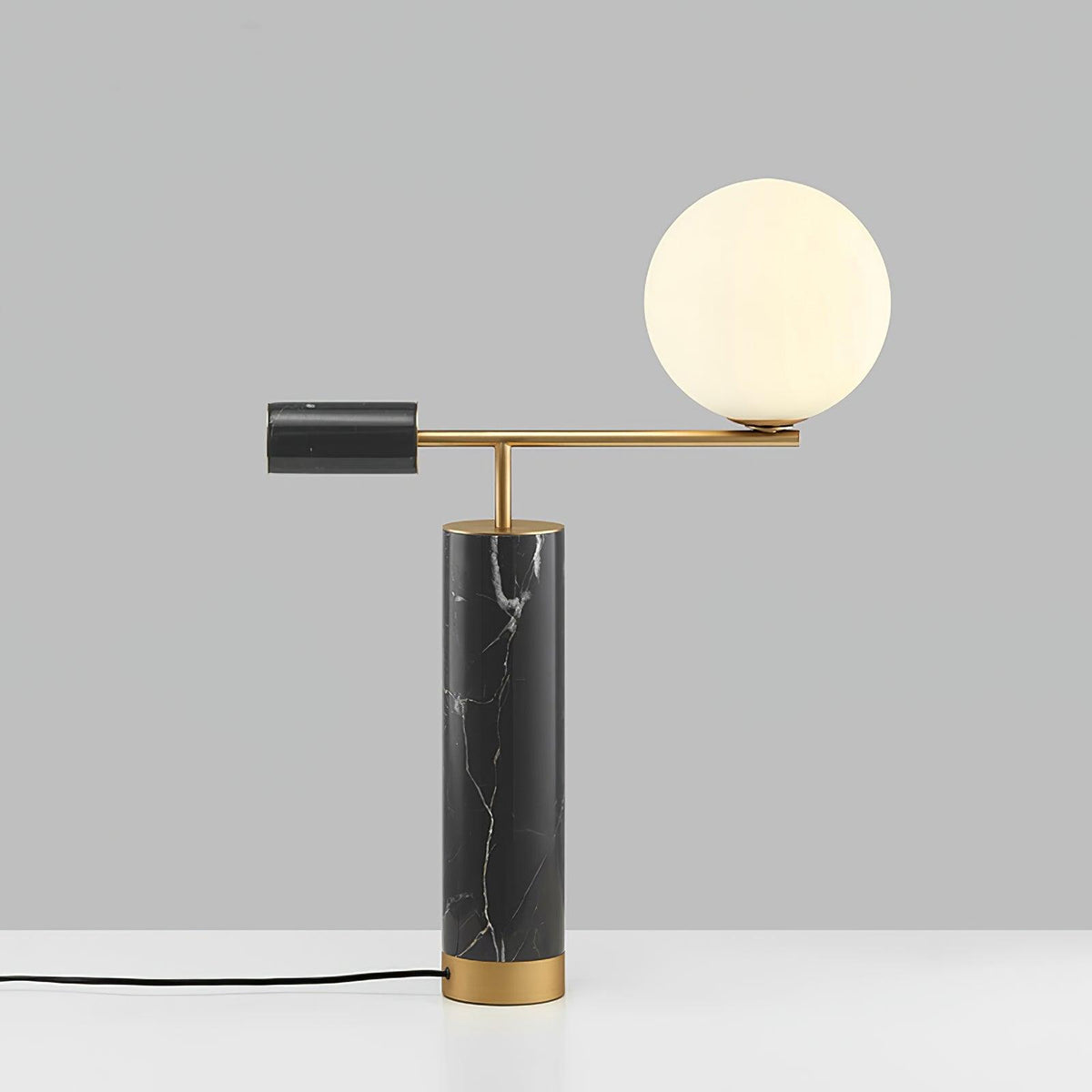 Photographed from a lower, tilted angle, the Clérachic lamp's brass arm carries its glass globe across a grey backdrop.