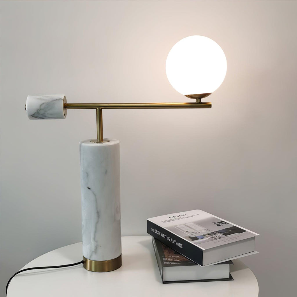 In its white marble finish, the lit Clérachic lamp stands beside two closed books on a round table against a pale wall.