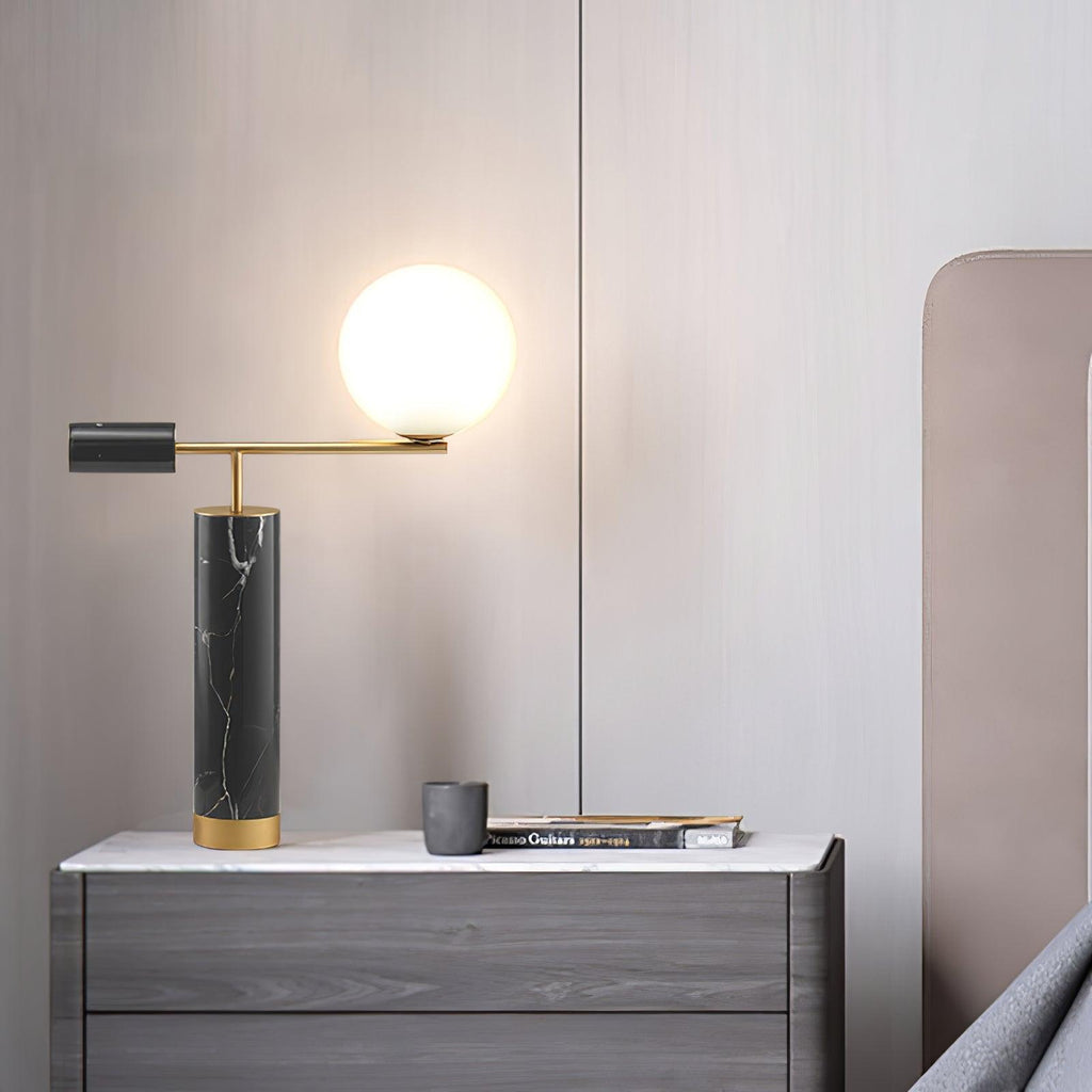 The lit Clérachic lamp sits on a grey wood dresser with a small mug and book, a blush pink headboard behind it.