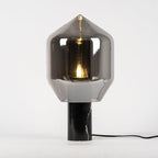 A Clérachic table lamp with a tall, pointed smoked-glass shade on a black veined marble base, shown at an angle.