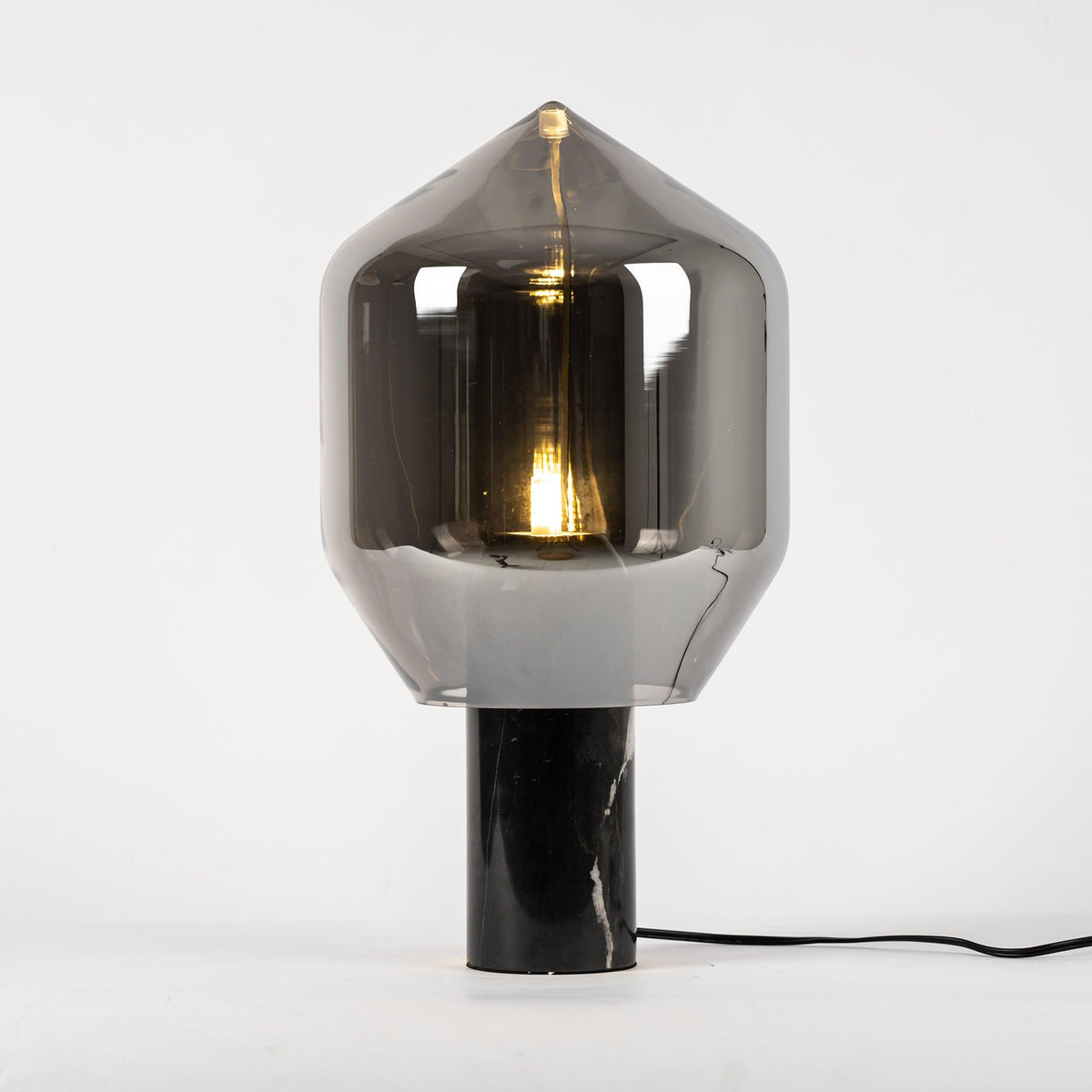 A Clérachic table lamp with a tall, pointed smoked-glass shade on a black veined marble base, shown at an angle.
