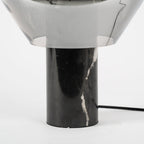 A close crop of the black veined marble base on a Clérachic table lamp, its cord trailing from the socket.
