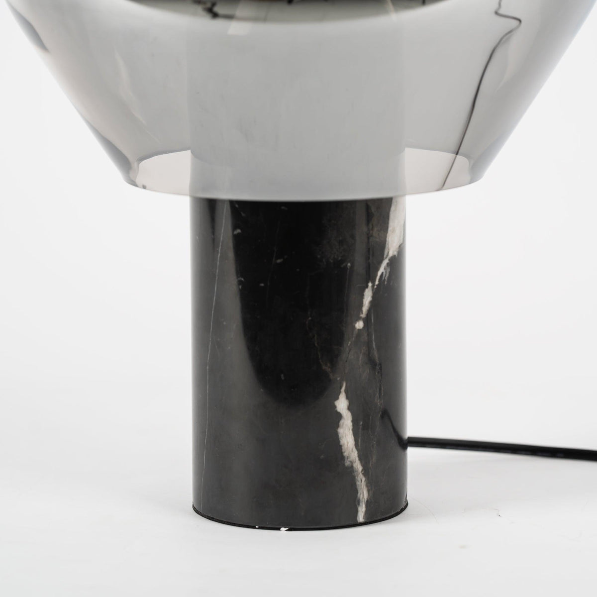 A close crop of the black veined marble base on a Clérachic table lamp, its cord trailing from the socket.