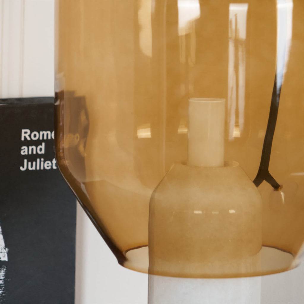 An extreme close-up of Clérachic's amber glass shade meeting its marble base, a book titled Romeo and Juliet behind it.
