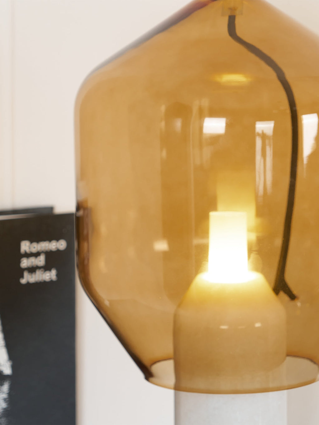 A close crop of Clérachic's amber glass shade, showing the seam line in the glass beside a book spine.