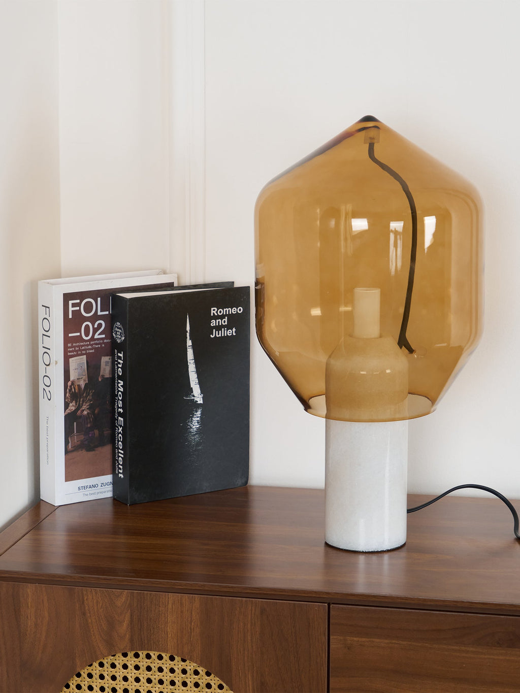 Clérachic's amber-glass table lamp on white marble, lit in a room corner beneath a white ceiling cornice.