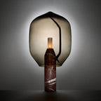 Clérachic's smoked-glass lamp on a dark veined marble base, glowing softly against a dramatic dark backdrop.