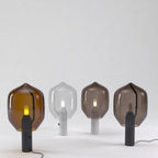Four Clérachic table lamps lined up, showing the amber and smoked glass shades over both black and marble bases.