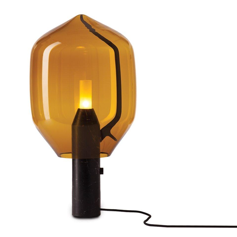 An amber-glass Clérachic table lamp on its black base, cord trailing across the floor in a plain white studio shot.