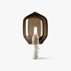 Clérachic's smoked-glass bedside lamp glowing softly on its white marble base, shot alone against a plain studio backdrop.