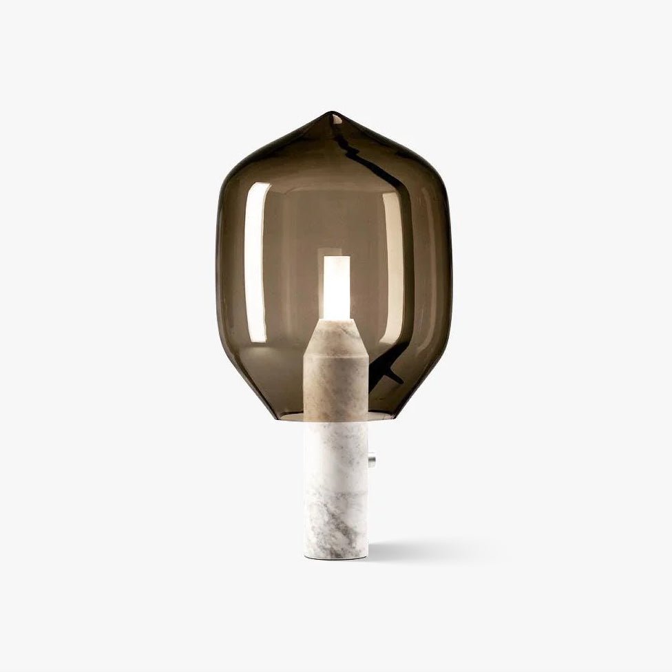 Clérachic's smoked-glass bedside lamp glowing softly on its white marble base, shot alone against a plain studio backdrop.