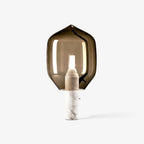 A smoked-glass Clérachic table lamp on a white marble base, standing alone with a soft shadow on a white backdrop.