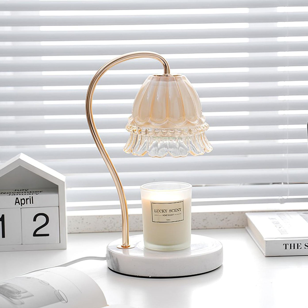 Next to a wooden desk calendar and a stack of books, this Clérachic candle warmer lamp's shade hangs over its candle jar.