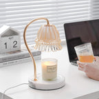 A hand holds a glass of iced drink beside this Clérachic candle warmer lamp, its laptop and desk calendar visible nearby.