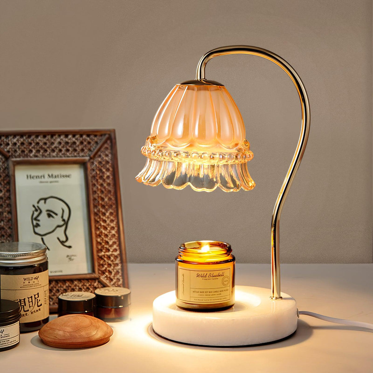 Against a beige wall beside a framed sketch, this Clérachic candle warmer lamp glows above an amber candle jar and small dish.