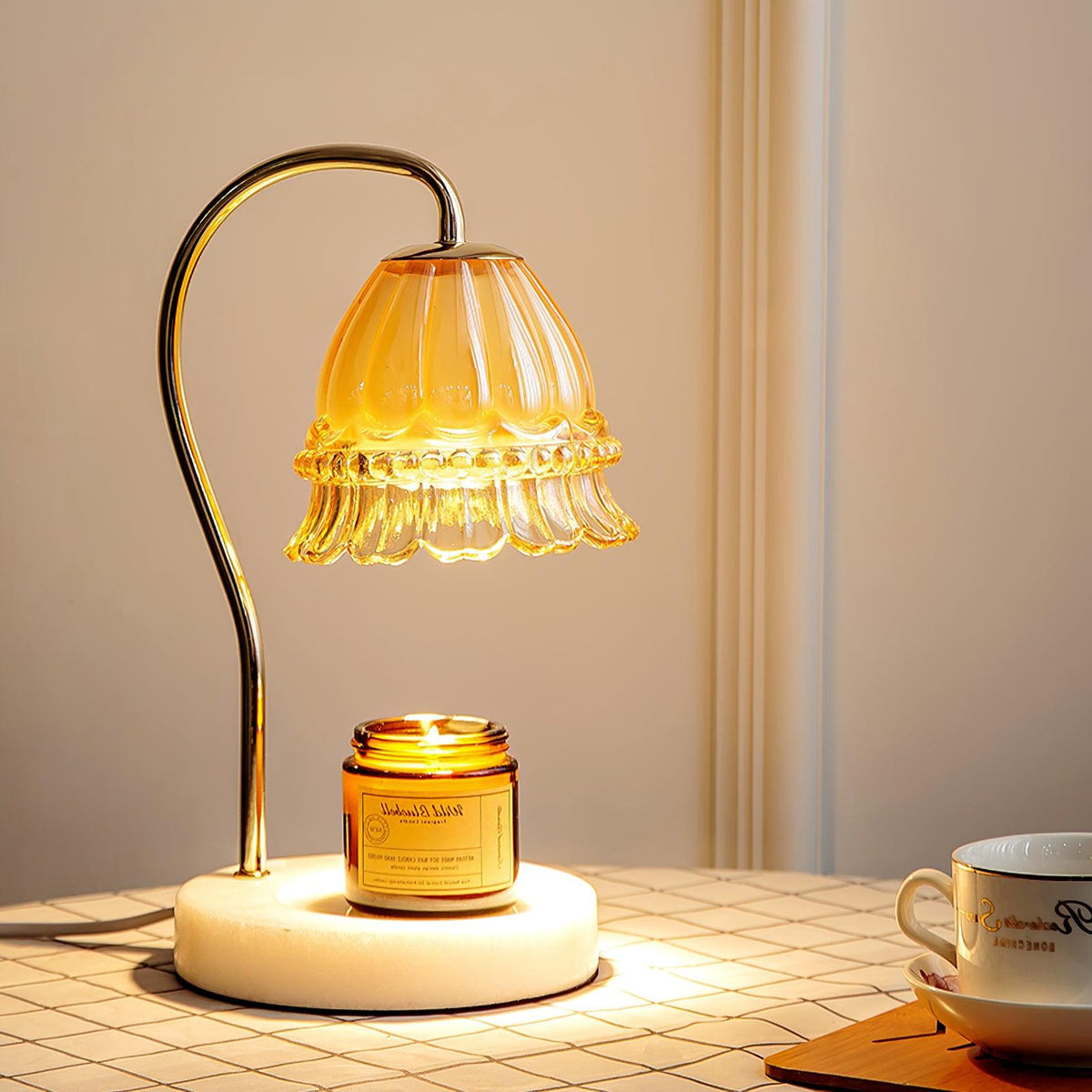 Glowing warmly on a checked tablecloth, this Clérachic candle warmer lamp lights its amber candle jar beside a teacup.