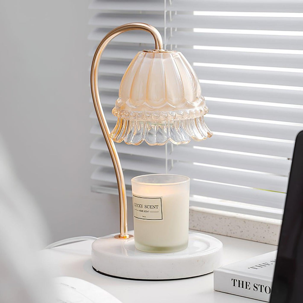 Beside venetian blinds and a stack of books, this Clérachic candle warmer lamp's glass shade sits above an unlit candle jar.