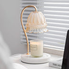 Beside venetian blinds and a stack of books, this Clérachic candle warmer lamp's glass shade sits above an unlit candle jar.
