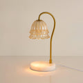 Lit softly against a plain warm backdrop, this Clérachic candle warmer lamp's glass shade glows above its round marble base.
