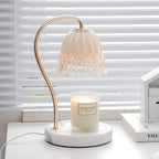 On a marble-topped bedside table near venetian blinds, this Clérachic candle warmer lamp sits beside a small stack of books.