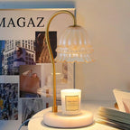 Against a mood board of fashion photos and an open laptop, this Clérachic candle warmer lamp glows over its glass candle jar.