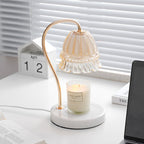 Beside a wooden desk calendar and venetian blinds, this Clérachic candle warmer lamp's amber glass shade glows over its candle.