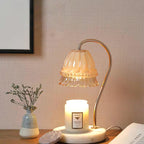 On a wood surface against linen wallpaper, this Clérachic candle warmer lamp stands near a small vase of dried flowers.