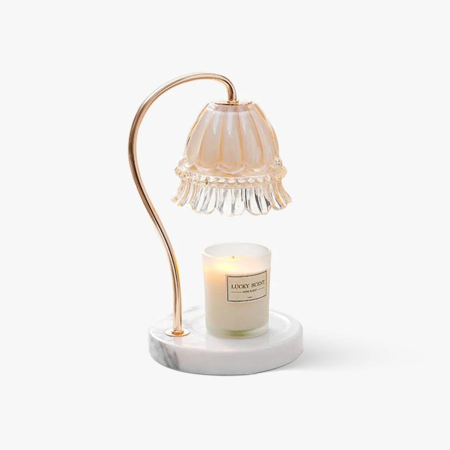 A curved gold arm suspends a ruffled glass flower shade above a lit candle jar on this Clérachic warmer lamp's round marble base.