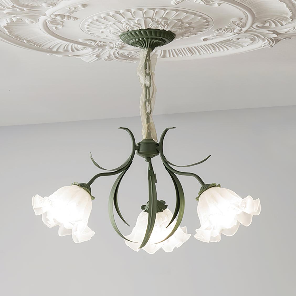 Seen in profile on a grey backdrop, the curved green arms of this Clérachic chandelier hold its shades to one side, unlit.