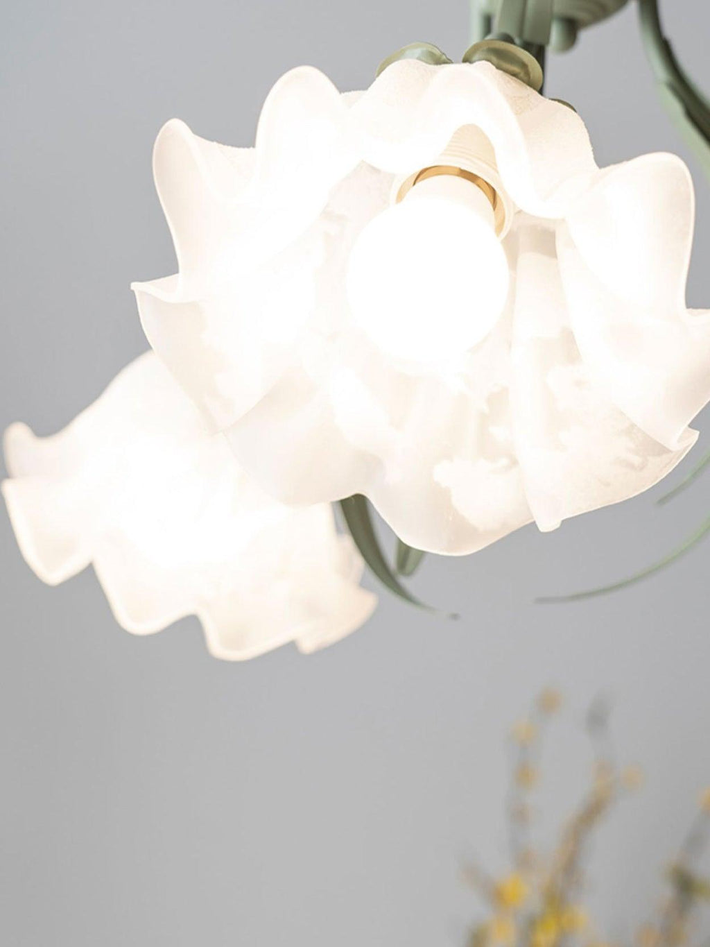 Close view of one ruffled white shade on this Clérachic chandelier, lit from within around its bulb.