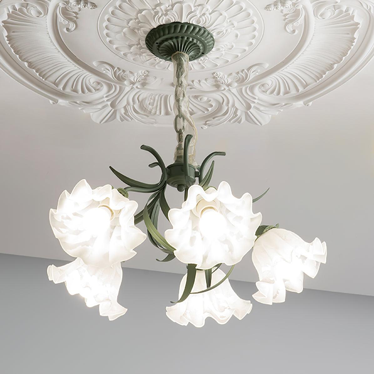 From a low angle on a grey backdrop, the green metal arms of this Clérachic chandelier arch beneath unlit white shades.