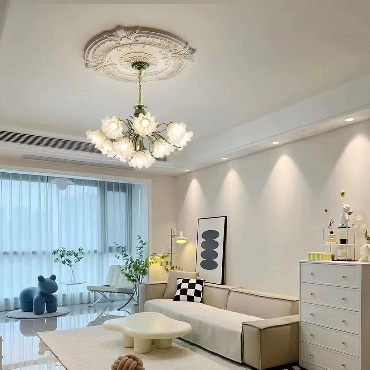 In a modern grey and white living room, this Clérachic chandelier hangs lit above a low sofa.