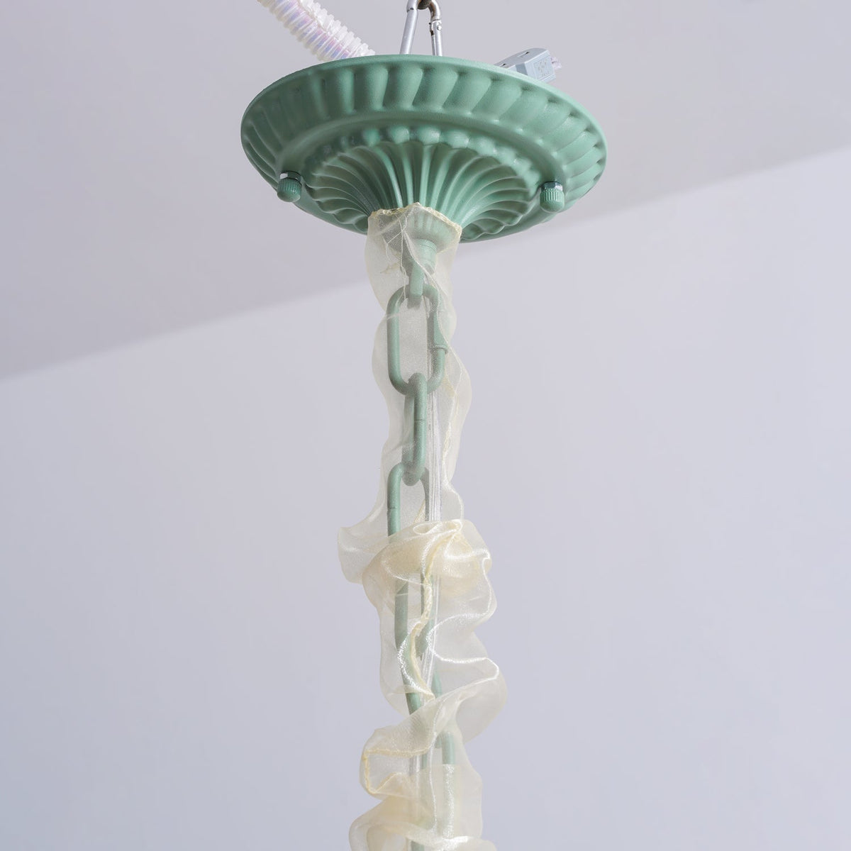 Close view of the ceiling mount on this Clérachic chandelier, its chain wrapped in sheer ivory fabric.